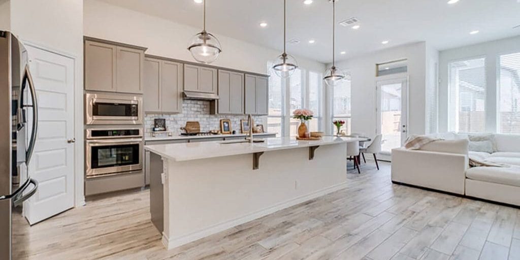 A modern kitchen with freshly painted gray cabinets, white quartz countertops, and stainless steel appliances showing the results of professional kitchen cabinet painting.